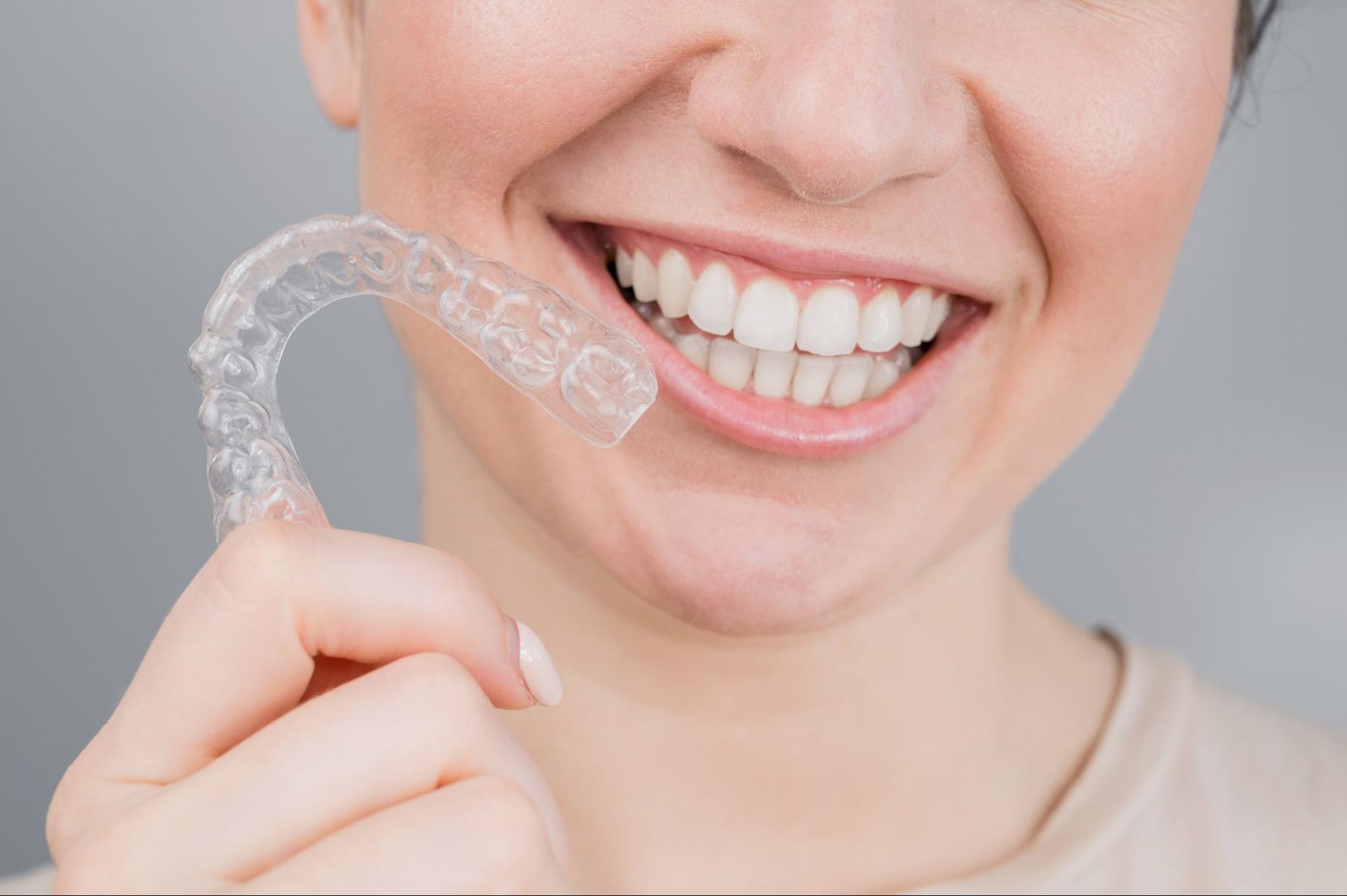 Smiling woman holding clear aligner, showcasing dental health and orthodontic care at Viva Orthodontics in Bountiful.