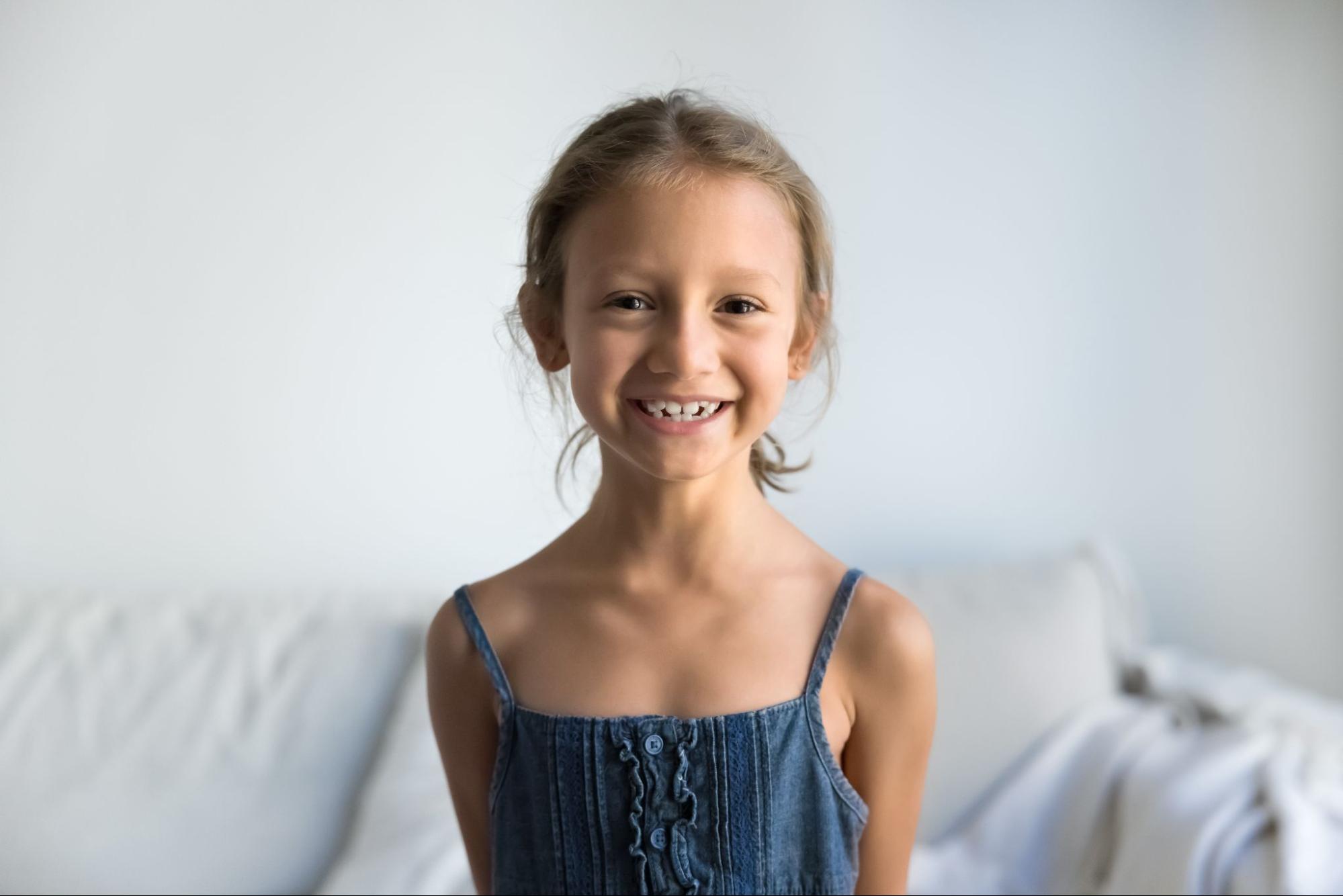 Smiling girl in casual attire showcasing healthy teeth, representing positive outcomes of orthodontic care at Viva Orthodontics in Bountiful, UT, emphasizing early evaluations and clear aligners.